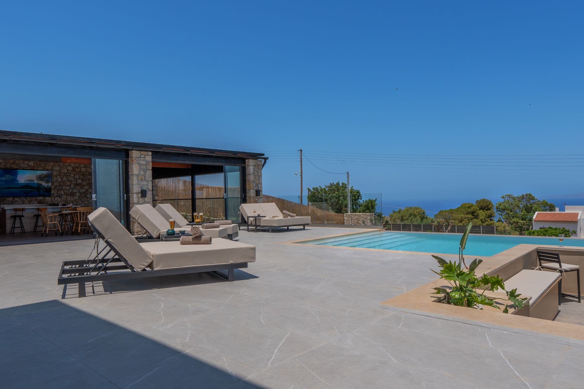 Pool terrace with loungers, ocean views stretching to distant islands, and manicured gardens
